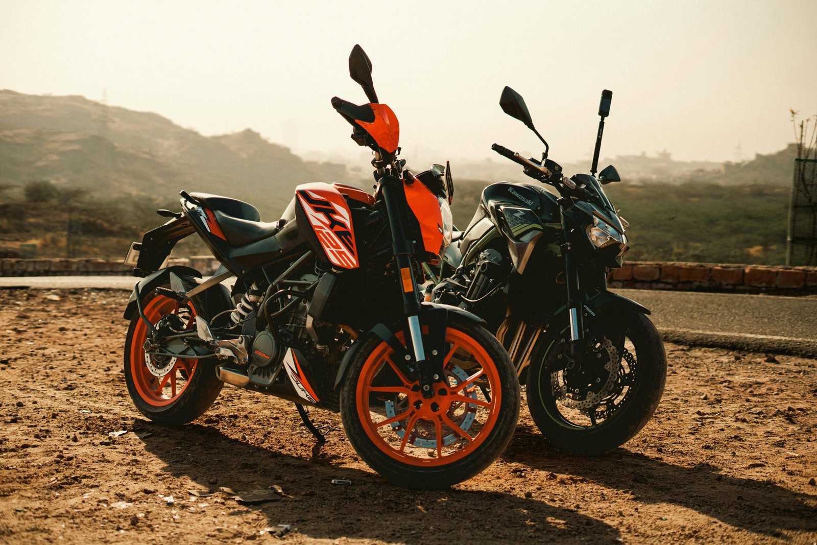 Two motorcycles parked outdoors in a rural desert area under sunny weather, showcasing adventure potential.